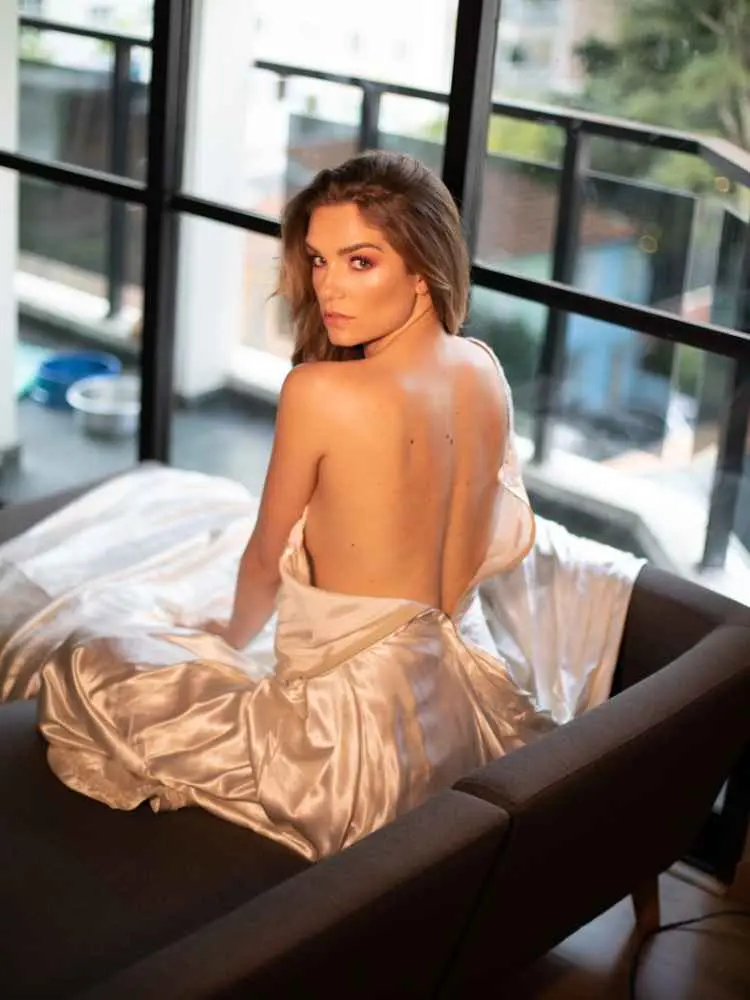 Mulher com mais de 30 anos em ensaio fotográfico, usando vestido de seda aberto nas costas sentada em sofá