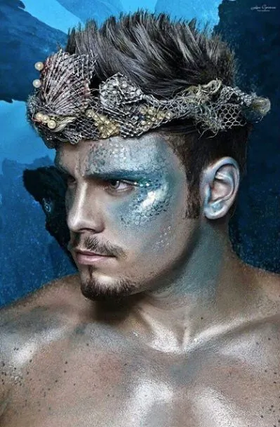 Homem de pele morena com maquiagem de sereia azul, com escamas e nadadeiras 