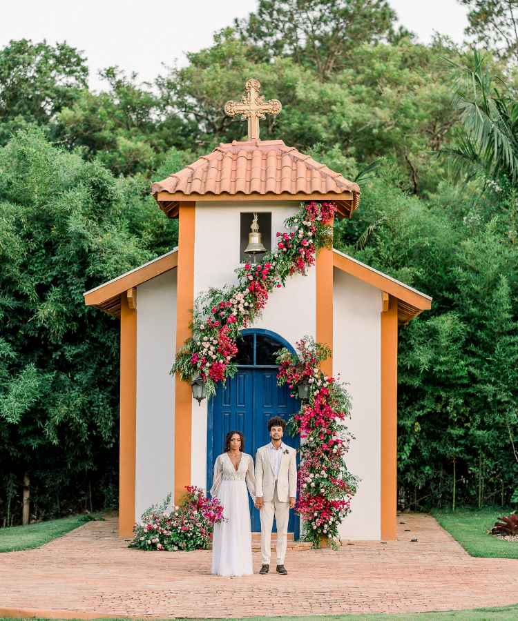 Noivos de frente à capela decorada com flores