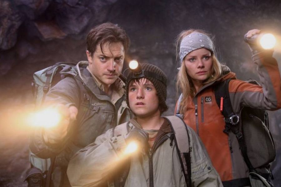 Foto de Brandan Fraser (Trevor), Josh Hutcherson (Sean) e Anita Briem (Hannah) de "Viagem Ao Centro Da Terra: O Filme". Eles estão com lanterna nas mãos e em local com pedras.