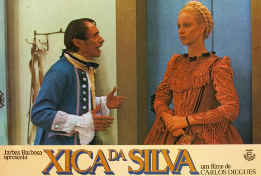 Cartaz colorido com a cena do filme "Xica da Silva", onde aparece Elke vestida com um traje de época vermelho e cabelo longo preso com tranças no topo de cabeça. Cartaz com a cena do filme "Xica da Silva", onde aparece Elke vestida com um traje de época vermelho e cabelo longo preso com tranças no topo de cabeça.