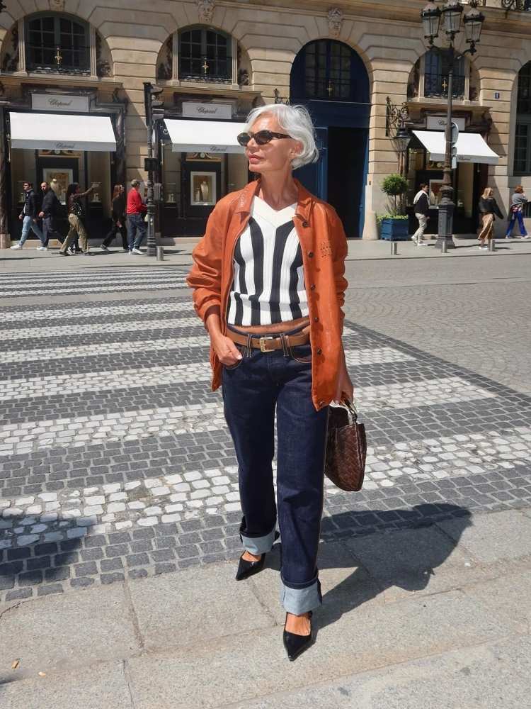 Senhora de pele clara usando blusa branca e preta, jaqueta laranja e calça jeans com barra dobrada