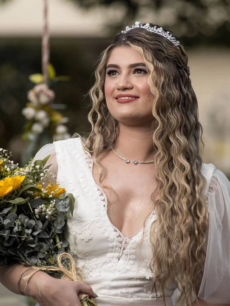 Mulher de pele clara com vestido de noiva, segurando buquê, com maquiagem minimalista e cabelo em triondas