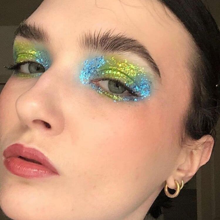 Mulher de pele clara com maquiagem de glitter azul e verde