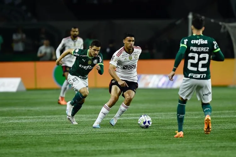 Victor Hugo, jogador do Flamengo, conduzindo a bola perto dos palmeirense Raphael Veiga e Piquerez.