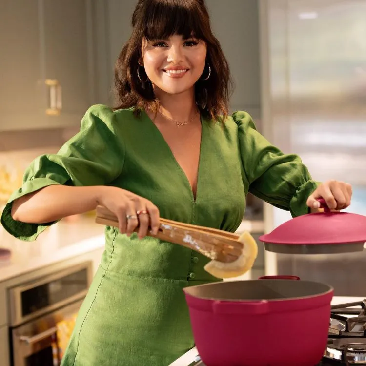 Uma foto da cantora e atriz Selena Gomez usando um vestido verde e cozinhando , com cabelo chanel e franja sobre a sobrancelha