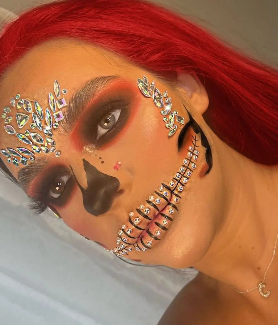 Pessoa de pele claea e cabelo vermelho usando maquiagem de caveira mexicana usando strass