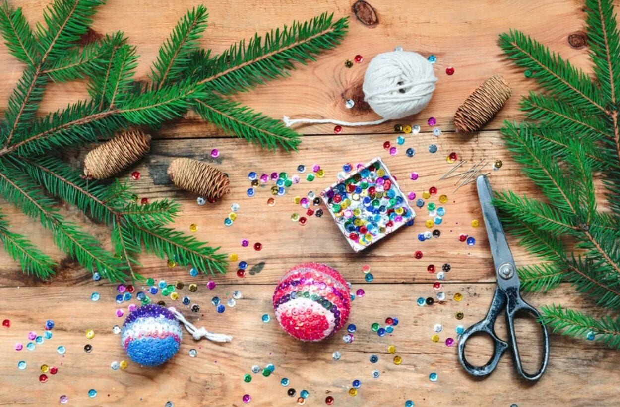 Mesa com partes de árvore de Natal, enfeites com lantejoulas, barbante, tesoura