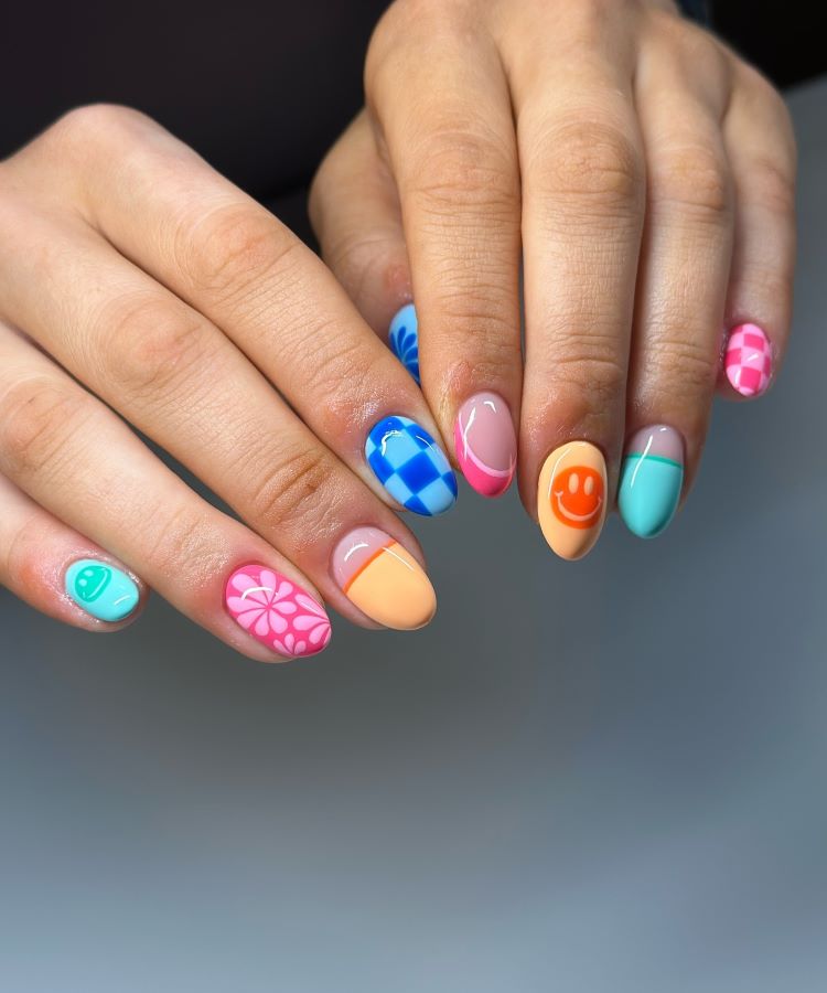 A imagem apresenta unhas de carnaval alegres e coloridas. Com formato oval, cada unha exibe designs distintos: sorrisos, flores, quadriculados e linhas geométricas. As tonalidades vibrantes, como azul, rosa, laranja e verde, criam um visual divertido, perfeito para festas.