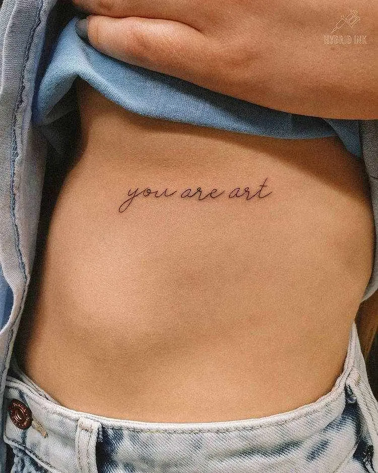 Tatuagem escrito "you are art" em fineline na costela