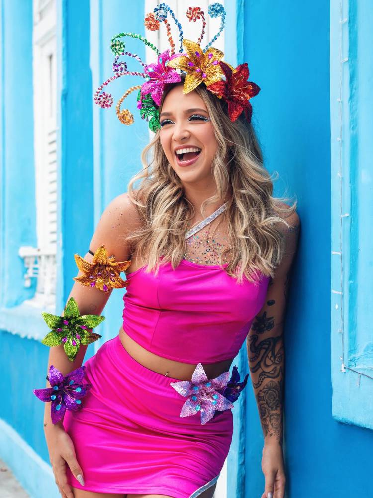 Mulher de pele clara e cabelo loiro com cropped e saia rosas, flores nos braços e no cabelo 