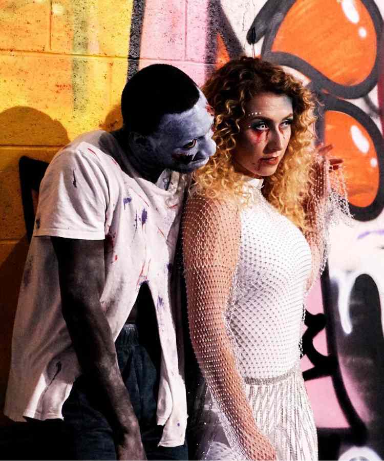 Fantasia de casal para o Halloween: Zumbi e Noiva Cadáver. Ele usa camiseta branca rasgada e maquiagem azul enquanto ela usa roupa branca e sangue falso nos olhos 