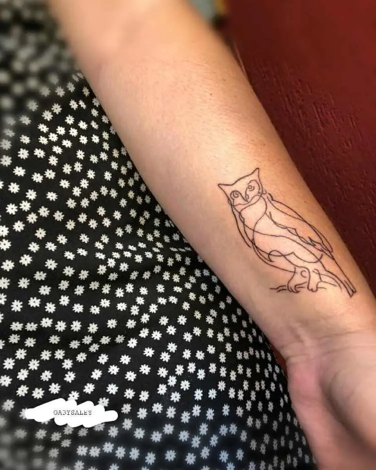 tatuagem de linha única de coruja na lateral do pulso de pessoa de pele clara que usa roupa preta com mini margaridas