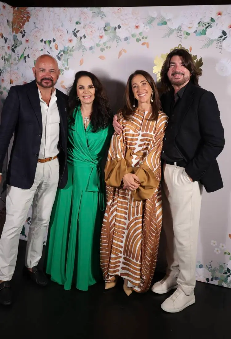 Pierre Martinez de look off-white com blazer preto, Cris Porto de verde, Bia Yunes de vestido branco e dourado e Stephane Rolland de terno preto e calça off-white em fundo com papel de parede com logo da Cris Porto joalheria e flores