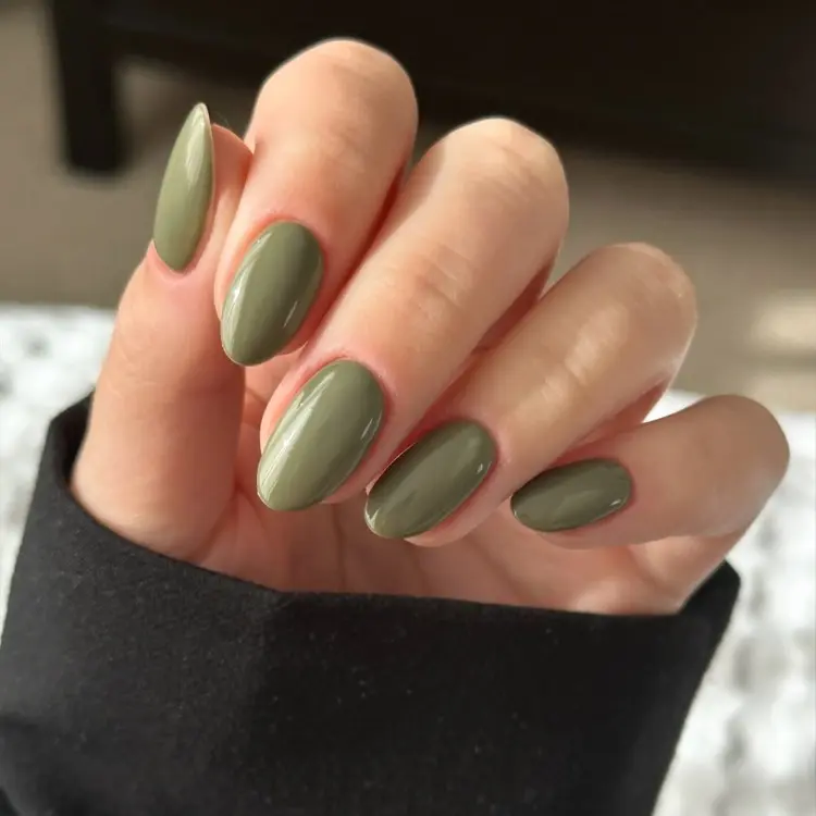 Mão de pele clara com manga preta e unhas almond curtas em verde oliva