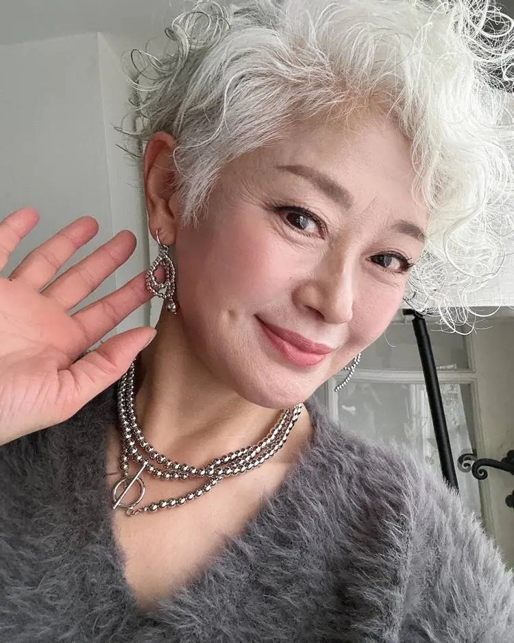 Mulher oriental com cabelos brancos, usando joias pratas e roupa de pelinho