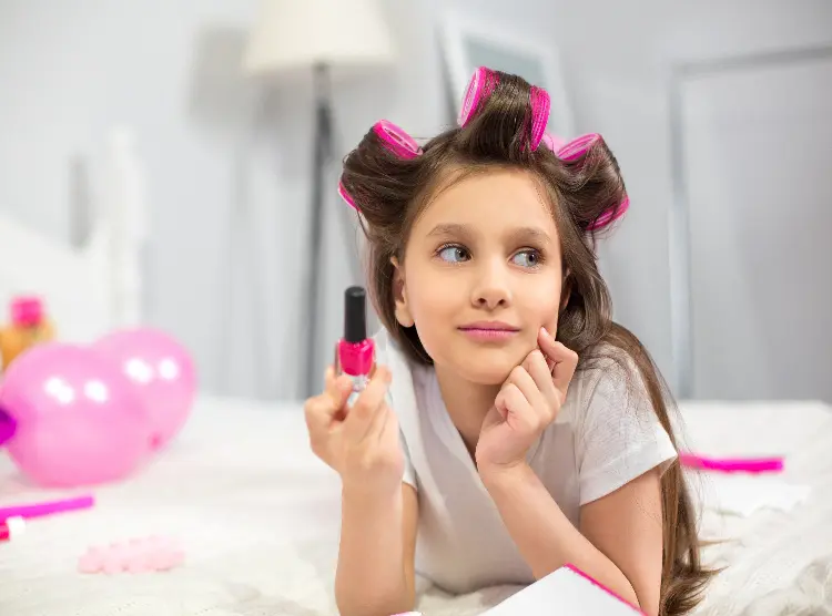 Menina com bobs no cabelo, enquanto segura um vidro de esmalte na mão