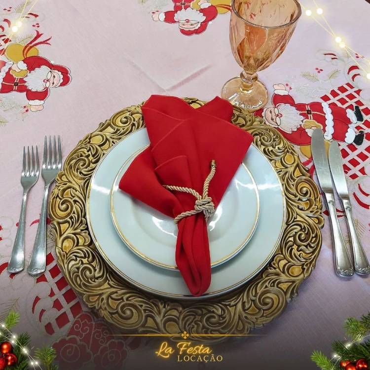 Sousplat dourado com pratos brancos e dourados e guardanapo vermelho.