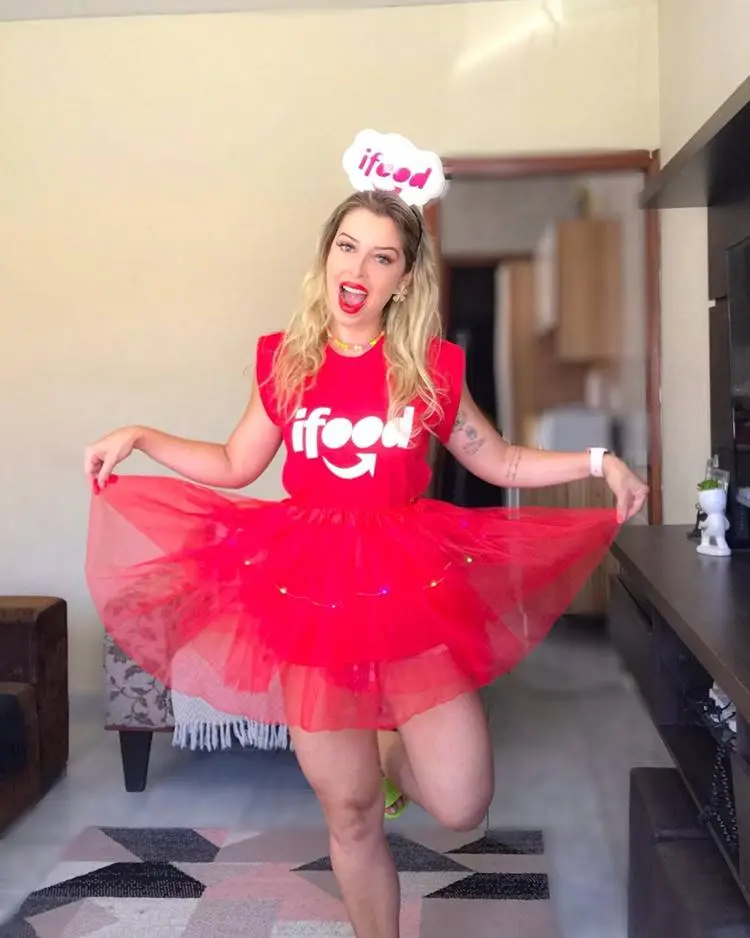 Mulher de pele clara com tiara Ifood, body vermelho Ifood e saia de tule vermelha