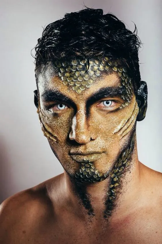 Homem de pele morena com maquiagem de sereia dourada, com escamas e nadadeiras 