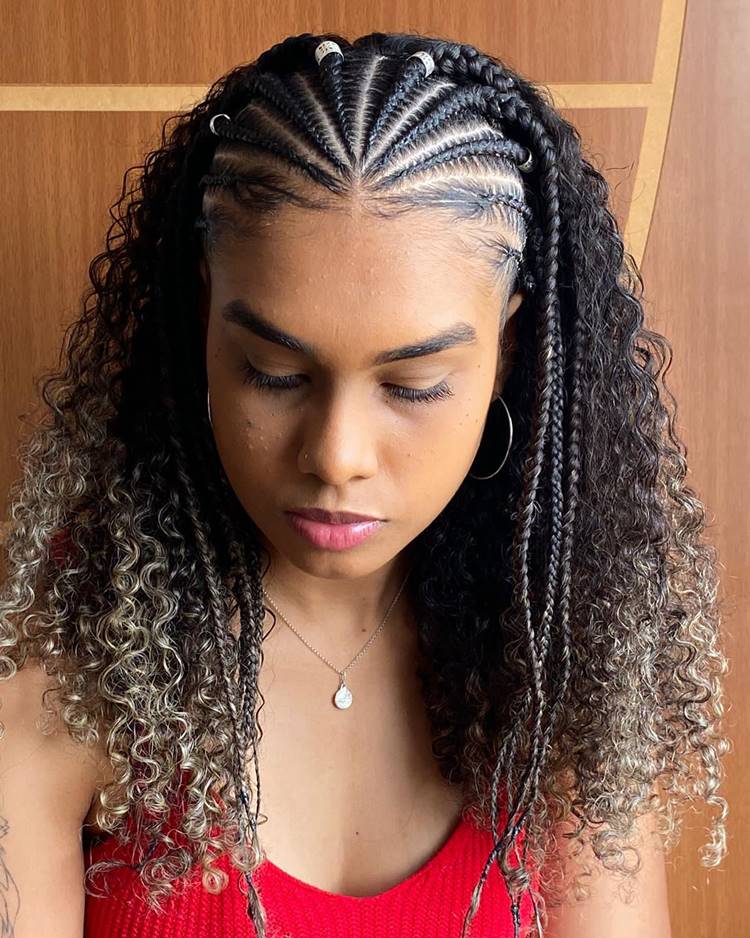 Trança africana com joia em topo de cabeça de cabelo cacheado. Menina está com olhos fechados, usa blusa vermelha e joias prateadas