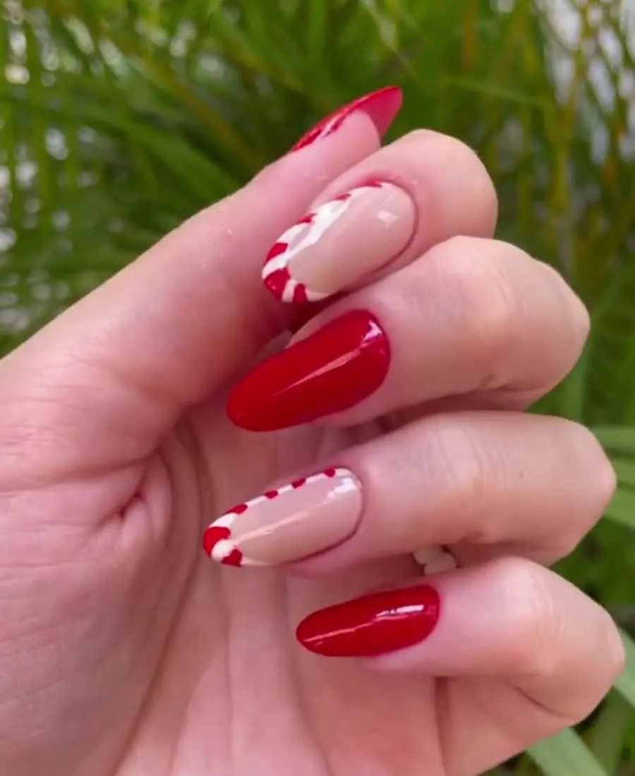 Mão de pessoa de pele clara com unha em formato almond, sendo algumas em vermelho e outras em nude com francesinha de bengala doce