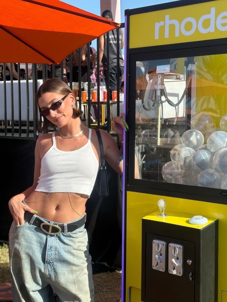 mulher usando regata branca cropped com calça jeans azul e cinto preto. usando oculos de sol, body chain e bolsa baguette preta