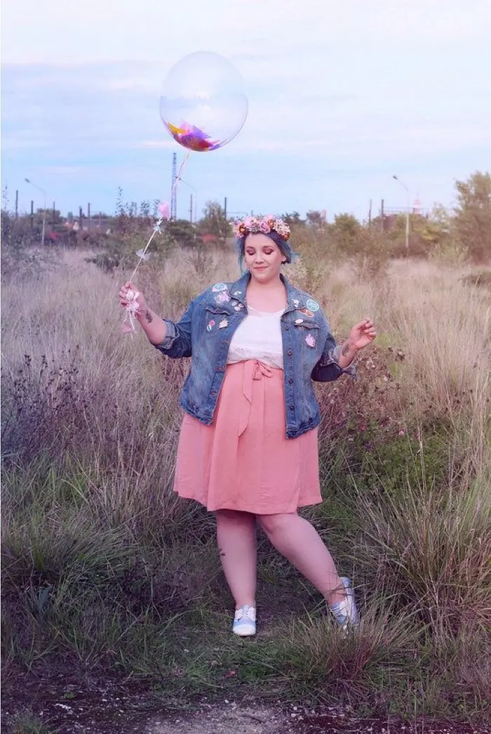 Frase para foto pensativa plus size segura balão, usa flores na cabeça e veste saia rodada goiaba, camisa branca, jaqueta jeans com detalhes de flor e tênis colorido Frase para foto pensativa plus size