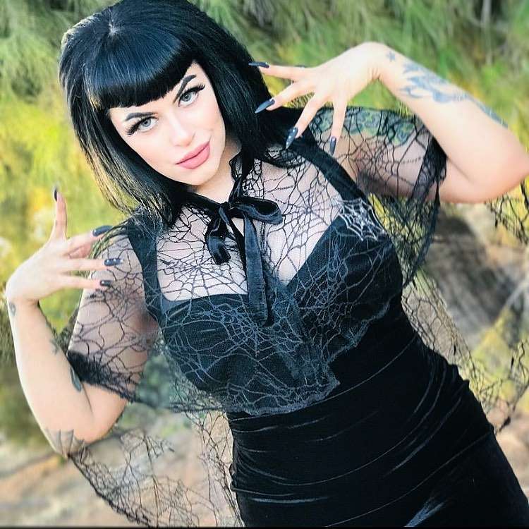 Mulher de pele clara usando vestido preto e capa transparente com teia 