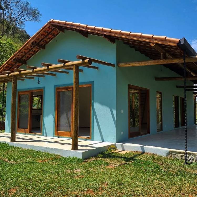 Imagem de fachada de casa simples de cor azul com portas de vidro. Na entrada, um pequeno pergolado decora