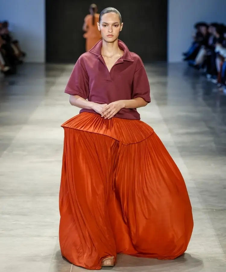Foto de modelo na passarela usando camisa polo rosa e saia volumosa laranja