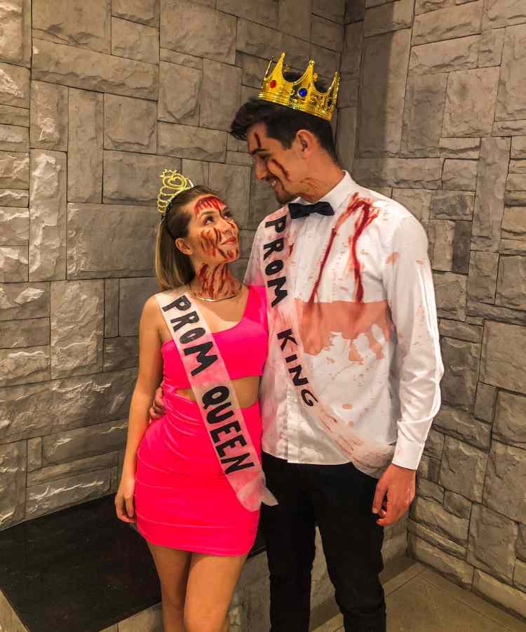 Fantasia de casal para o Halloween: Rainha e Rei do Baile. Ela usa vestido rosa, coroa, sangue falso e faixa "prom queen". Já ele usa camisa branca com sangue falso, calça preta, coroa e faixa "prom king"