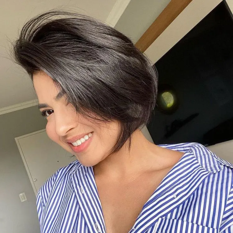 Uma mulher de pele clara com um corte de cabelo curto repicado usando uma camisa listrada branca e azul
