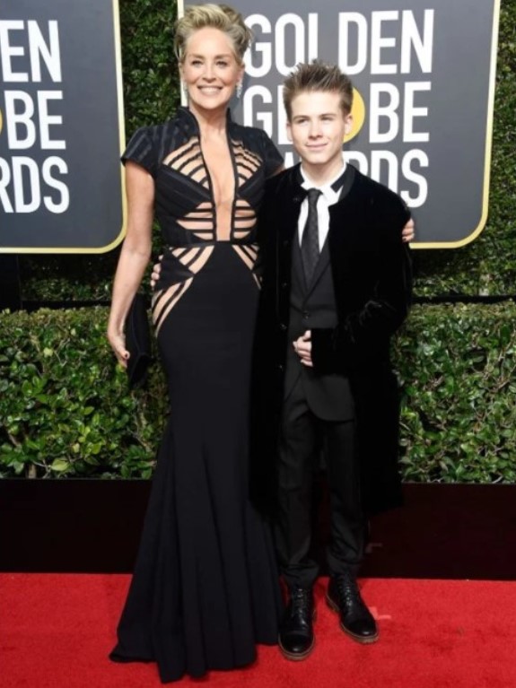 Sharon Stone posando no Globo de Ouro de 2018 com um vestido de Vitor Zerbinato ao lado de Roan Joseph Bronstein. 