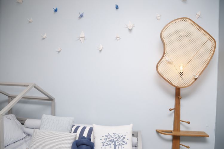 Quarto com parede azul clara, cama cinza com almofadas e origamis na parede