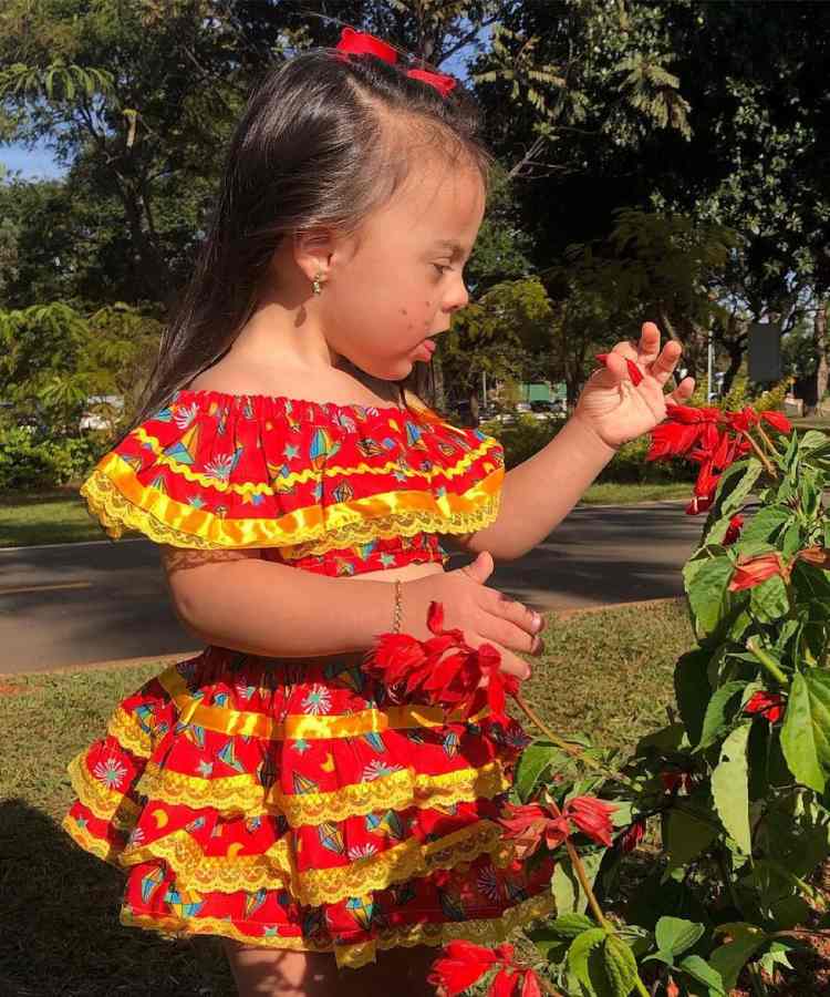 Menina com vestidinho clássico de festa junina, vermelho com estampa de balão, babados e renda amarela