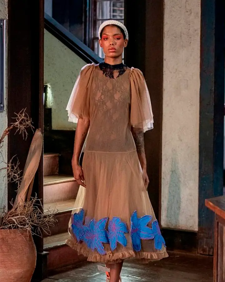 Modelo usando um vestido bege de mangas e detalhes azuis.
