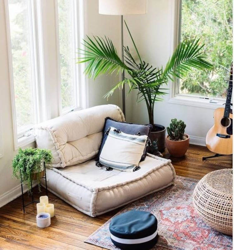 Espaço zen com grande almofada bege com encosto, puffes, velas, plantas, violão e janelas