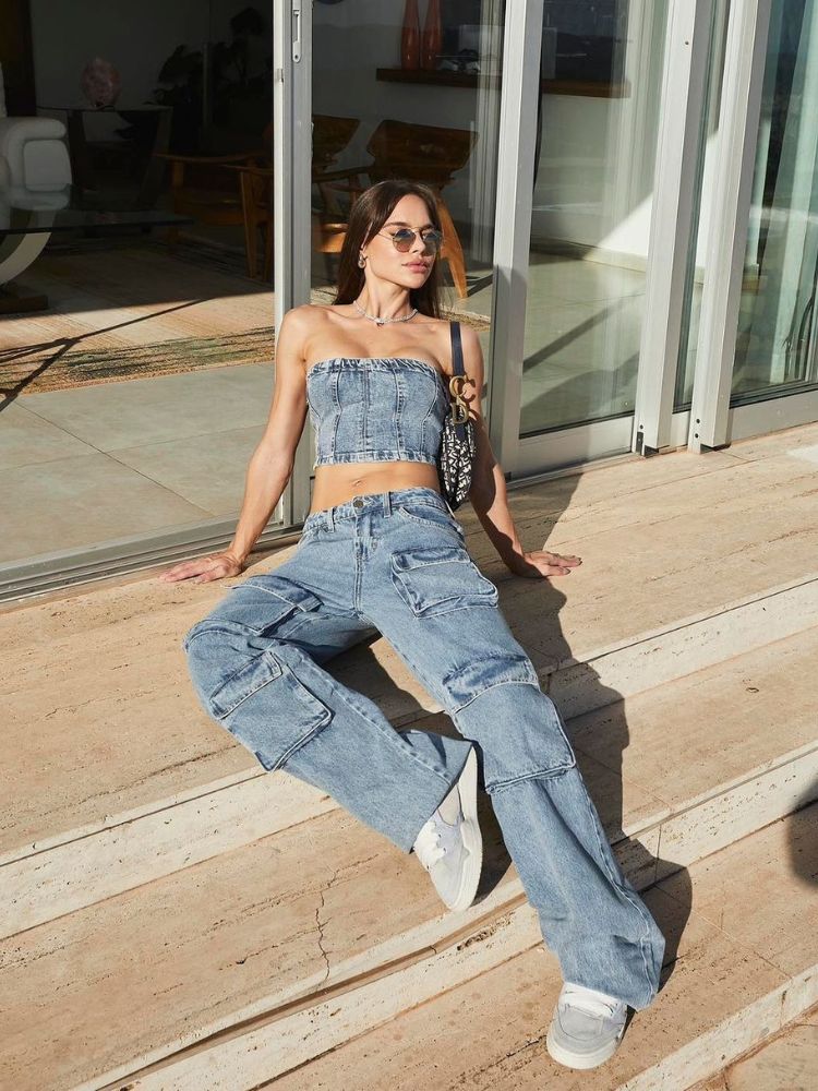 Mulher de pele clara sentada nos degraus de uma escada usando cropped jeans e calça jeans cargo, repleta de bolsos