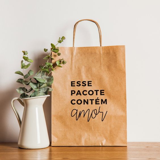 Sacola de papel escrito "Esse pacote contém amor" ao lado de uma jarra com galhos de planta sob uma mesa de madeira