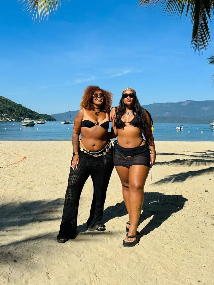 Mari Lobo e Ana Flávia na praia usando biquíni e saídas de praia pretos