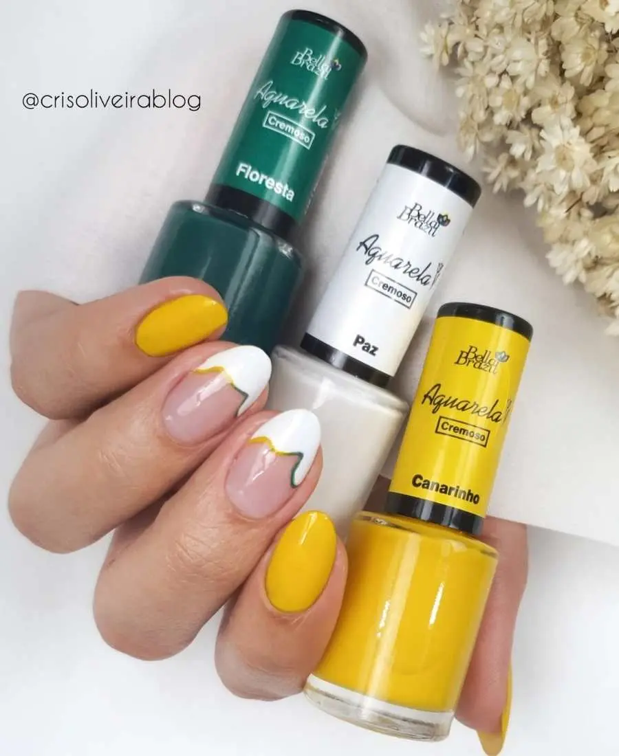 Imagem de mão com unhas decoradas para a Copa do Mundo 2022. Cores usadas: verde, amarelo e branco da marca Bella Brazil. Arte, desenho abstrato branco com acabamento amarelo e verde.