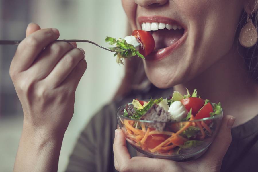 Mulher comendo pote de salada para curar ressaca de Ano Novo.