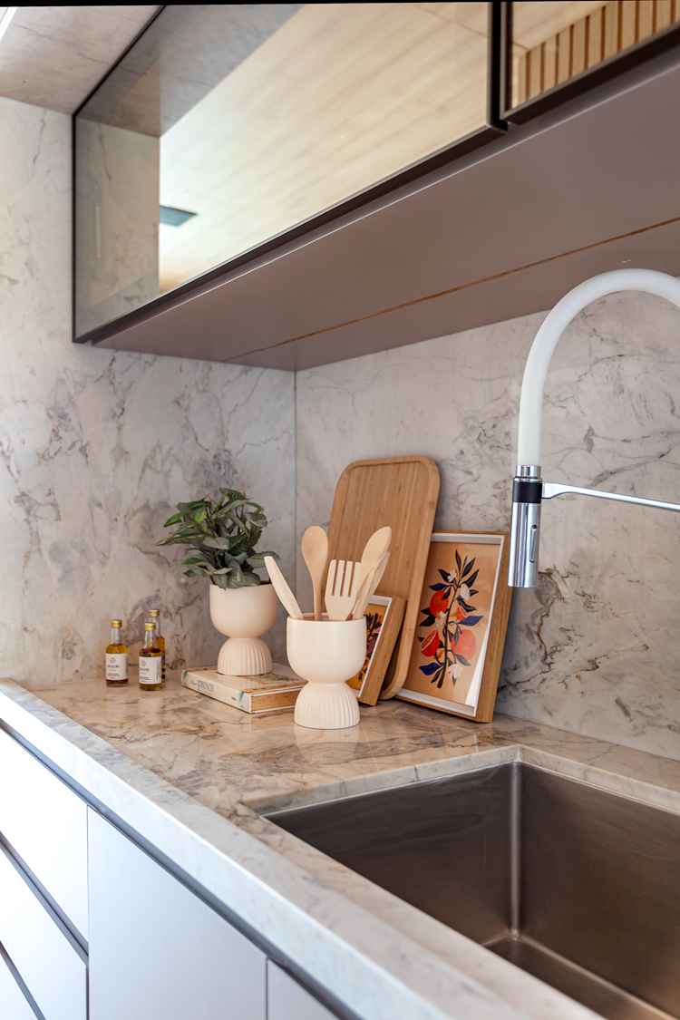 foto de bancada de pia da cozinha com mármore claro, itens decorativos em bege e madeira, vaso de planta e torneira branca