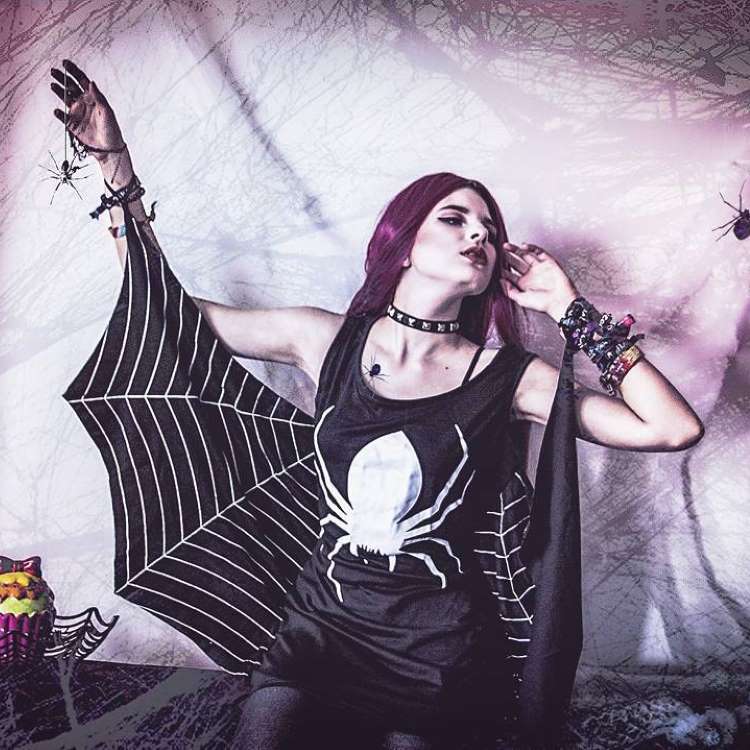 Menina com capa teia de aranha que vai na mão e vestido preto com desenho de aranha branca 