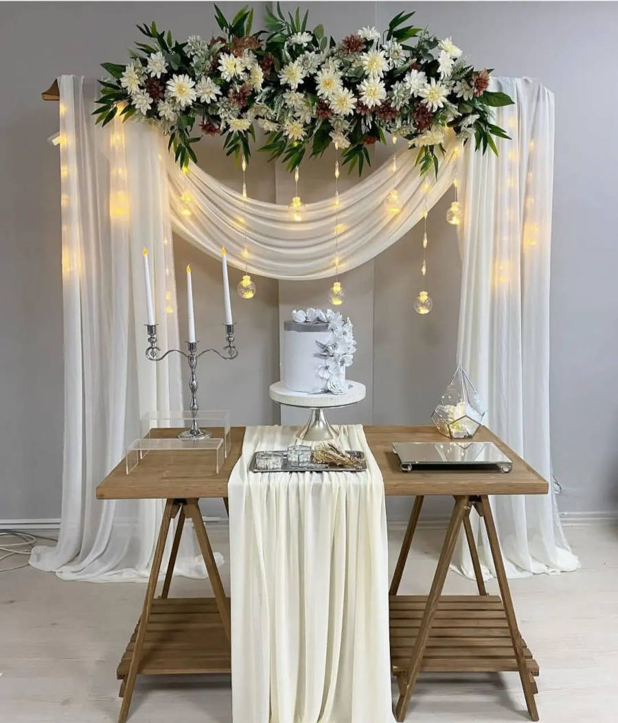 Fundo decorado com lâmpadas penduradas, arranjo de flores e cortina.