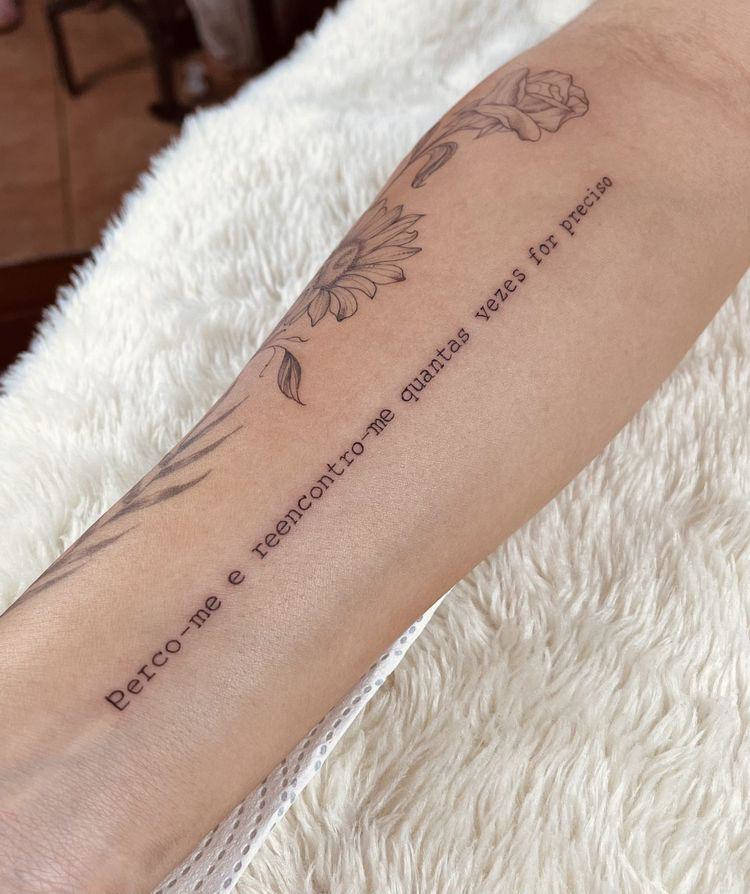 braço tatuado com flores e frase "perco-me e reencontro-me quantas vezes for preciso"
