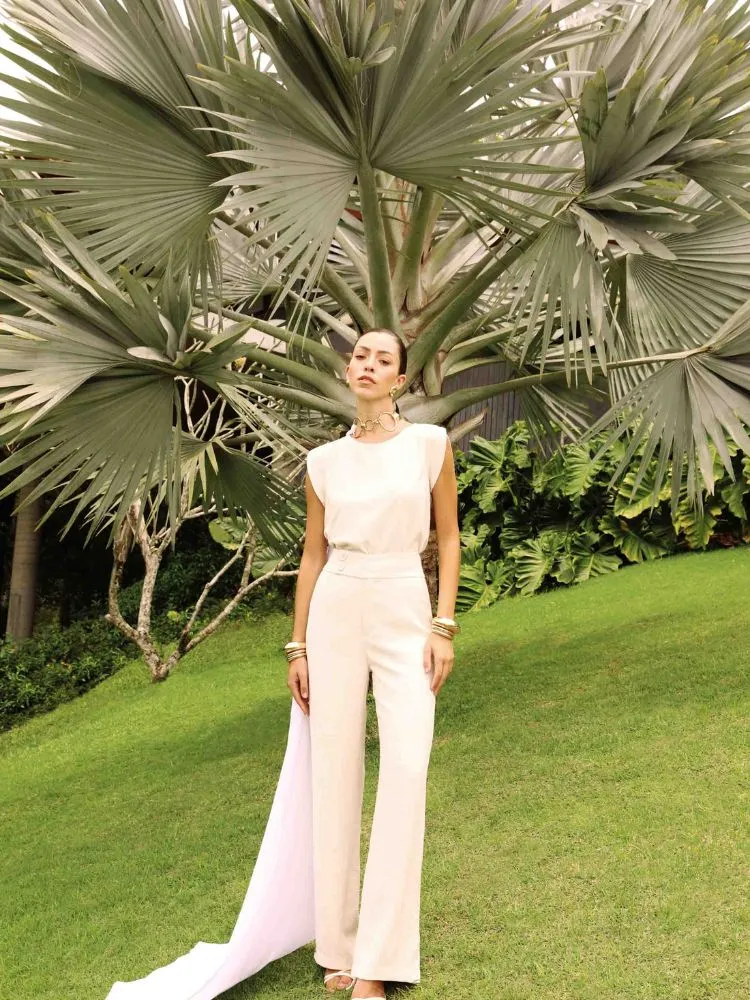 uma modelo loira posa em um jardim, ela usa um conjunto branco de calça e blusa da coleção dias dourados da DIMY