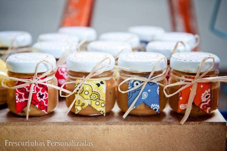 A imagem representa doce de leite em pote de vidro decorado com bandeirinha e fio de palha