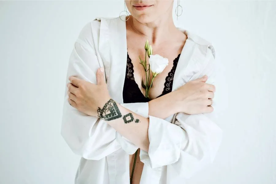 mulher com flor branca no top preto. Por cima, ela usa uma camisa branca 